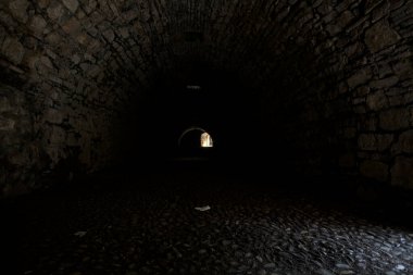 Karanlıkta kemer geçidi, güneş ışığı deliklerden geçiyor ve uzaklarda bir açıklık var.