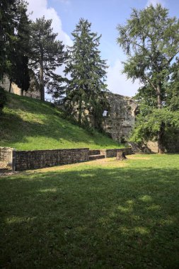 Etrafını çevreleyen ağaçlarla çevrili çimenler ve ağaçların arkasında bir şatonun kalıntıları olan gölgeler.