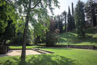 Etrafını çevreleyen ağaçlarla çevrili çimenler ve ağaçların arkasında bir şatonun kalıntıları olan gölgeler.