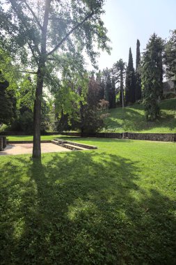 Etrafını çevreleyen ağaçlarla çevrili çimenler ve ağaçların arkasında bir şatonun kalıntıları olan gölgeler.