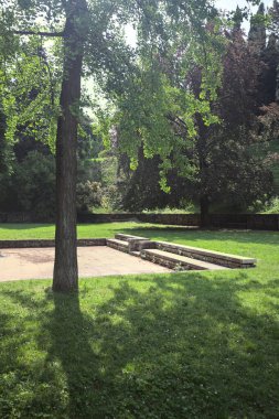 Etrafını çevreleyen ağaçlarla çevrili çimenler ve ağaçların arkasında bir şatonun kalıntıları olan gölgeler.