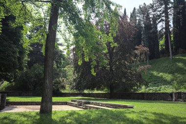 Etrafını çevreleyen ağaçlarla çevrili çimenler ve ağaçların arkasında bir şatonun kalıntıları olan gölgeler.