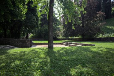 Etrafını çevreleyen ağaçlarla çevrili çimenler ve ağaçların arkasında bir şatonun kalıntıları olan gölgeler.