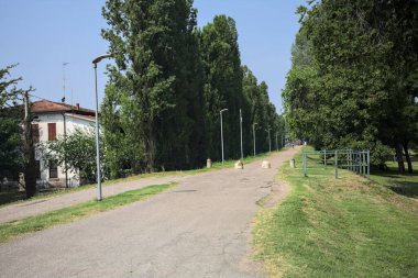 Güneşli bir günde, parkın kenarında kavak ağaçlarıyla çevrili bir toprak setin üzerinde, başlangıcının yanında bir ev olan bir patika.