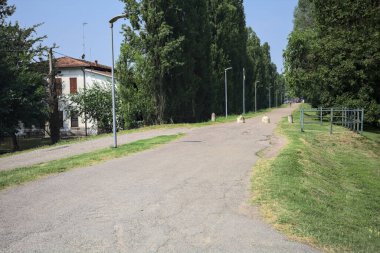 Güneşli bir günde, parkın kenarında kavak ağaçlarıyla çevrili bir toprak setin üzerinde, başlangıcının yanında bir ev olan bir patika.
