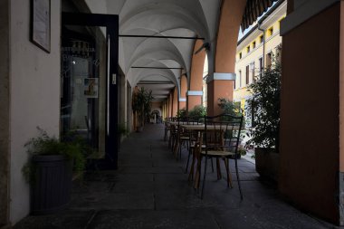 Güneşli bir günde, bir İtalyan kasabasında, üzerinde masalar ve sandalyeler olan bir sokağın kenarındaki gölgede.
