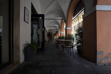 Güneşli bir günde, bir İtalyan kasabasında, üzerinde masalar ve sandalyeler olan bir sokağın kenarındaki gölgede.