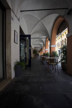 Güneşli bir günde, bir İtalyan kasabasında, üzerinde masalar ve sandalyeler olan bir sokağın kenarındaki gölgede.