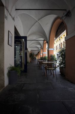 Güneşli bir günde, bir İtalyan kasabasında, üzerinde masalar ve sandalyeler olan bir sokağın kenarındaki gölgede.