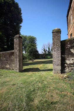 Bir şatonun kenarındaki patika, uzaktaki bir köprünün kemerlerinin altından geçiyor, yere düşen ağaçların gölgeleriyle.