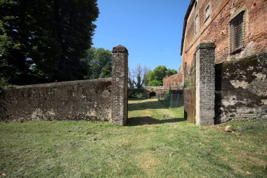 Bir şatonun kenarındaki patika, uzaktaki bir köprünün kemerlerinin altından geçiyor, yere düşen ağaçların gölgeleriyle.