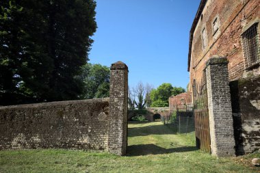 Bir şatonun kenarındaki patika, uzaktaki bir köprünün kemerlerinin altından geçiyor, yere düşen ağaçların gölgeleriyle.