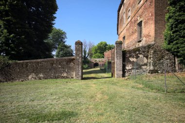Bir şatonun kenarındaki patika, uzaktaki bir köprünün kemerlerinin altından geçiyor, yere düşen ağaçların gölgeleriyle.
