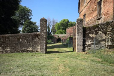 Bir şatonun kenarındaki patika, uzaktaki bir köprünün kemerlerinin altından geçiyor, yere düşen ağaçların gölgeleriyle.