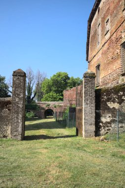 Bir şatonun kenarındaki patika, uzaktaki bir köprünün kemerlerinin altından geçiyor, yere düşen ağaçların gölgeleriyle.