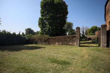 Bir şatonun kenarındaki patika, uzaktaki bir köprünün kemerlerinin altından geçiyor, yere düşen ağaçların gölgeleriyle.