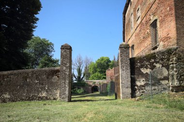 Bir şatonun kenarındaki patika, uzaktaki bir köprünün kemerlerinin altından geçiyor, yere düşen ağaçların gölgeleriyle.