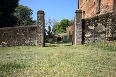 Bir şatonun kenarındaki patika, uzaktaki bir köprünün kemerlerinin altından geçiyor, yere düşen ağaçların gölgeleriyle.