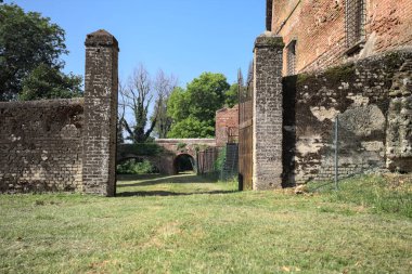 Bir şatonun kenarındaki patika, uzaktaki bir köprünün kemerlerinin altından geçiyor, yere düşen ağaçların gölgeleriyle.