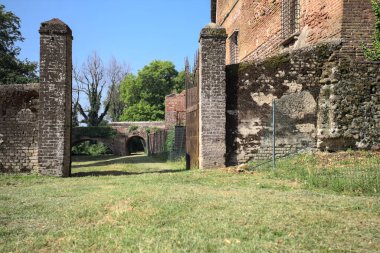 Bir şatonun kenarındaki patika, uzaktaki bir köprünün kemerlerinin altından geçiyor, yere düşen ağaçların gölgeleriyle.