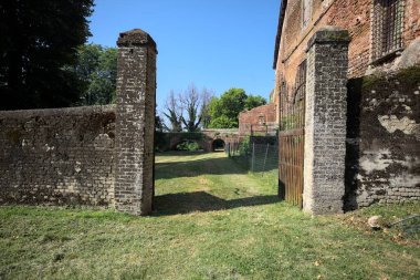 Bir şatonun kenarındaki patika, uzaktaki bir köprünün kemerlerinin altından geçiyor, yere düşen ağaçların gölgeleriyle.