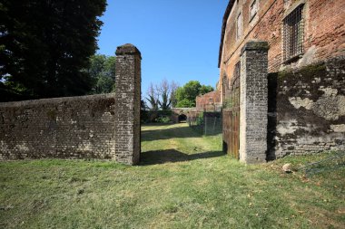 Bir şatonun kenarındaki patika, uzaktaki bir köprünün kemerlerinin altından geçiyor, yere düşen ağaçların gölgeleriyle.