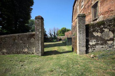 Bir şatonun kenarındaki patika, uzaktaki bir köprünün kemerlerinin altından geçiyor, yere düşen ağaçların gölgeleriyle.