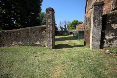 Bir şatonun kenarındaki patika, uzaktaki bir köprünün kemerlerinin altından geçiyor, yere düşen ağaçların gölgeleriyle.