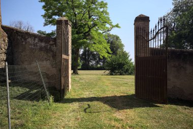 İtalya kırsalında güneşli bir günde, üzerinde ağaçlar olan bir çimenliğe açılan bir duvarın kapısını aç.