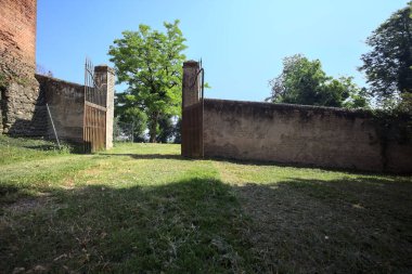 İtalya kırsalında güneşli bir günde, üzerinde ağaçlar olan bir çimenliğe açılan bir duvarın kapısını aç.