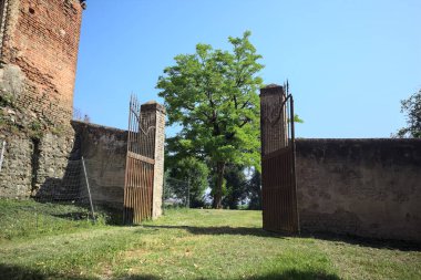 İtalya kırsalında güneşli bir günde, üzerinde ağaçlar olan bir çimenliğe açılan bir duvarın kapısını aç.