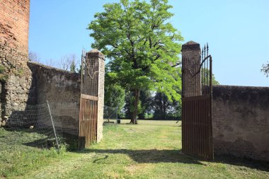 İtalya kırsalında güneşli bir günde, üzerinde ağaçlar olan bir çimenliğe açılan bir duvarın kapısını aç.