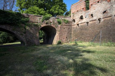 İtalya kırsalında güneşli bir günde terk edilmiş bir kalenin yanındaki tuğla köprünün altından geçen patika.