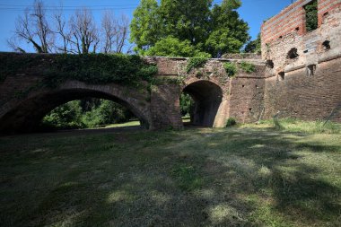İtalya kırsalında güneşli bir günde terk edilmiş bir kalenin yanındaki tuğla köprünün altından geçen patika.