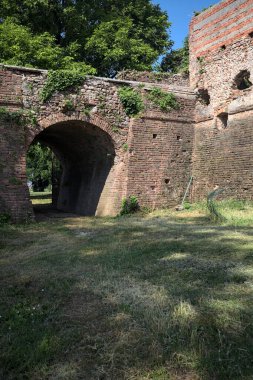 İtalya kırsalında güneşli bir günde terk edilmiş bir kalenin yanındaki tuğla köprünün altından geçen patika.
