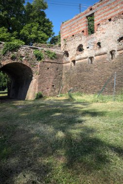 İtalya kırsalında güneşli bir günde terk edilmiş bir kalenin yanındaki tuğla köprünün altından geçen patika.