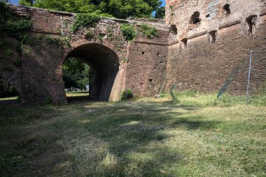 İtalya kırsalında güneşli bir günde terk edilmiş bir kalenin yanındaki tuğla köprünün altından geçen patika.