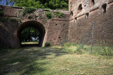 İtalya kırsalında güneşli bir günde terk edilmiş bir kalenin yanındaki tuğla köprünün altından geçen patika.