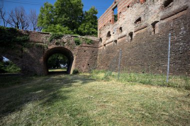 İtalya kırsalında güneşli bir günde terk edilmiş bir kalenin yanındaki tuğla köprünün altından geçen patika.