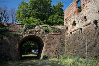 İtalya kırsalında güneşli bir günde terk edilmiş bir kalenin yanındaki tuğla köprünün altından geçen patika.