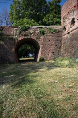 İtalya kırsalında güneşli bir günde terk edilmiş bir kalenin yanındaki tuğla köprünün altından geçen patika.