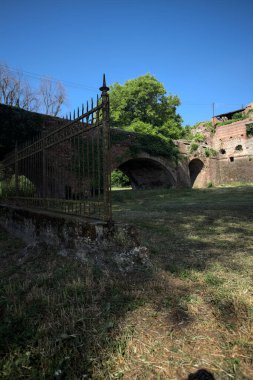 Terk edilmiş bir kalenin dış cephesi ve köprüsü güneşli bir günde İtalya kırsalında bir çitin arkasında görüldü.