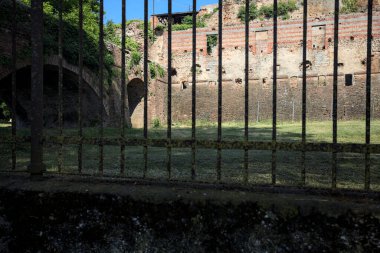 Terk edilmiş bir kalenin dış cephesi ve köprüsü güneşli bir günde İtalya kırsalında bir çitin arkasında görüldü.