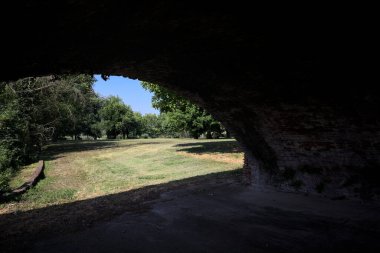 Güneşli bir günde çimenli bir bahçede, tuğla bir kemerin altından çerçevelenmiş ve görünür.
