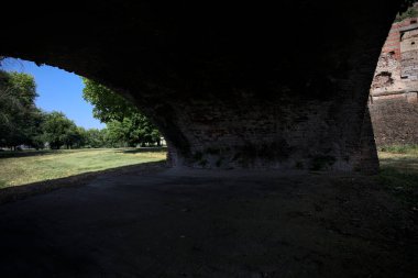 Güneşli bir günde çimenli bir bahçede, tuğla bir kemerin altından çerçevelenmiş ve görünür.