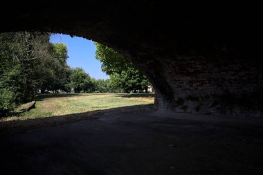 Güneşli bir günde çimenli bir bahçede, tuğla bir kemerin altından çerçevelenmiş ve görünür.