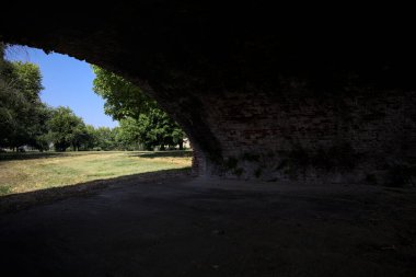 Güneşli bir günde çimenli bir bahçede, tuğla bir kemerin altından çerçevelenmiş ve görünür.
