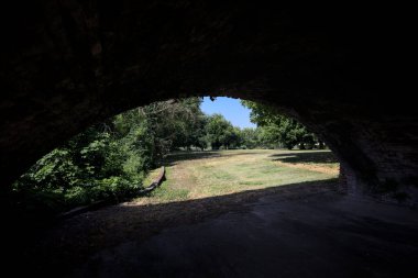 Güneşli bir günde çimenli bir bahçede, tuğla bir kemerin altından çerçevelenmiş ve görünür.
