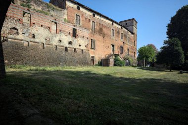 Terk edilmiş bir şatonun cephesi ve önünde bir çimen. Güneşli bir günde bir kemer tarafından çerçevelenmiş.