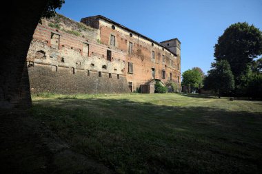 Terk edilmiş bir şatonun cephesi ve önünde bir çimen. Güneşli bir günde bir kemer tarafından çerçevelenmiş.